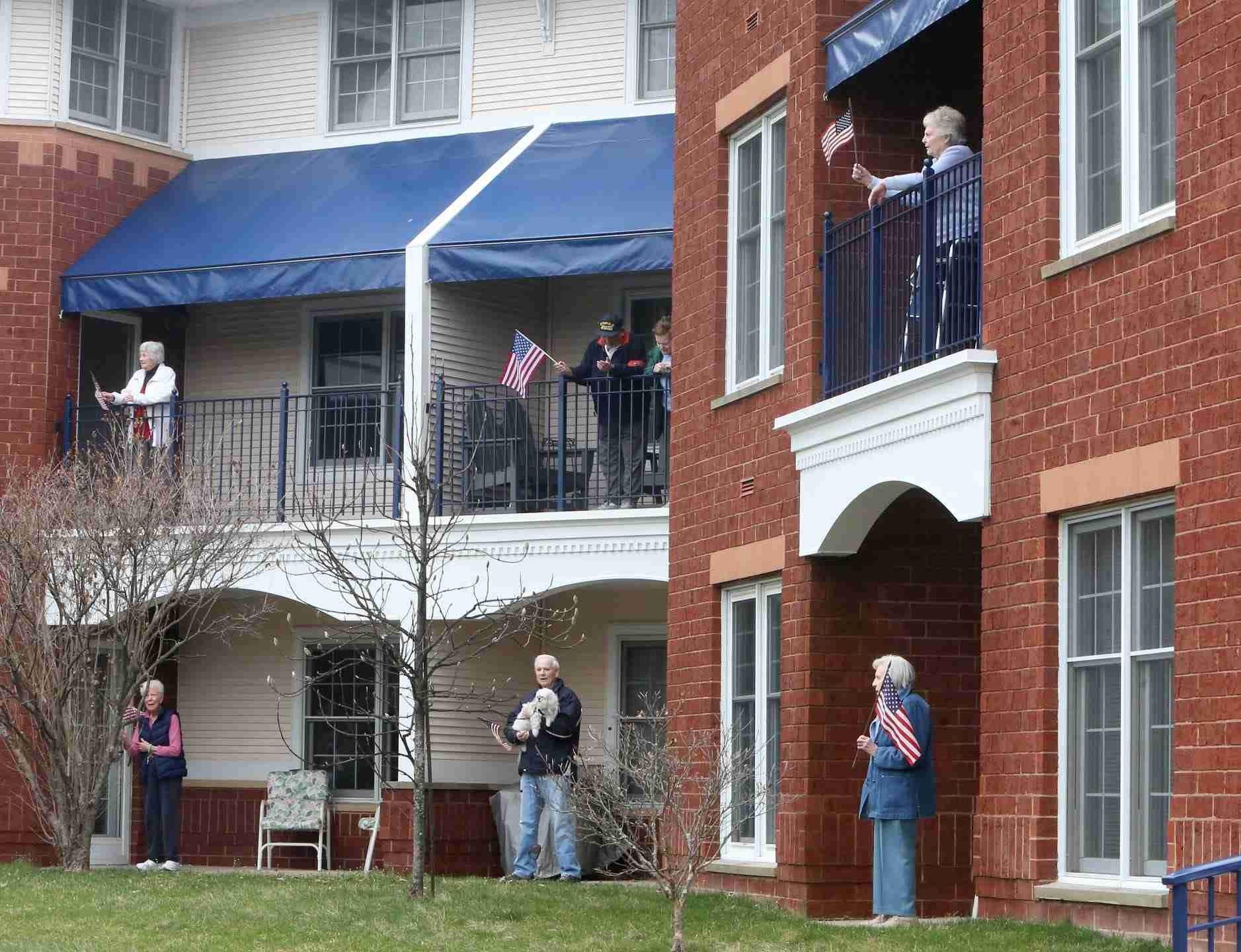 Residents at The Waterford at St. Luke Senior Independent Living Community emerge from their apartments to wave flags and sing "God Bless America" on their balconies and porches in North Canton, Ohio on Tuesday, March 24, 2020. In the wake of the coronavirus crisis, they must remain in their living areas. 