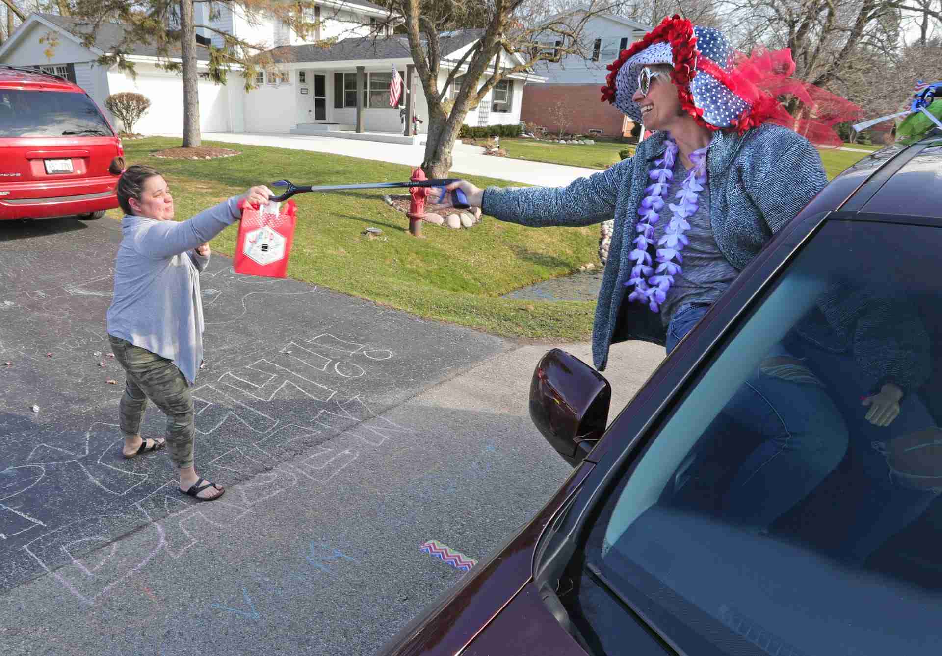 Becky Kops, right, uses a picker to hand her friend, Dajen Bohachek, a present as friends of Bohachek, of Bayside, held a social distance drive by birthday party for her during the coronavirus to celebrate her 44th birthday in Bayside, Wis. on Friday, April 3, 2020. The group decorated their vehicles at the Fox Point Village Hall before heading to Bohachek’s home to celebrate from the road. The stay at home order and the necessity to stay socially distant from each other has inspired creative ways for people to connect. 