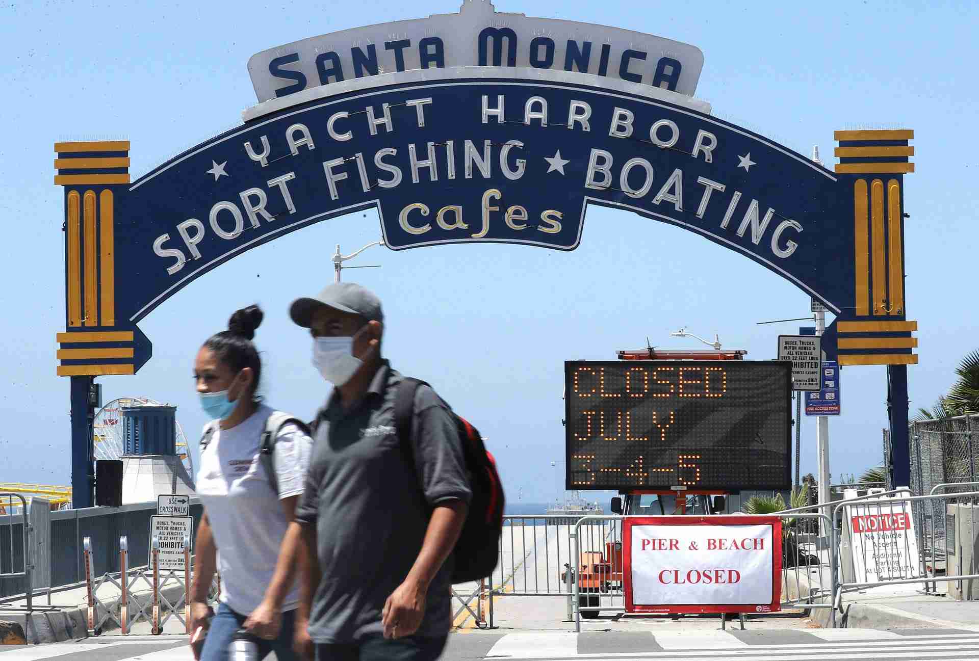 People wearing face coverings walk past the closed Santa Monica Pier amid the COVID-19 pandemic on July 3, 2020 in Santa Monica, California. Los Angeles County beaches and piers will be closed starting today through the July 4th holiday weekend amid some reinstated restrictions intended to slow the spread of the coronavirus.