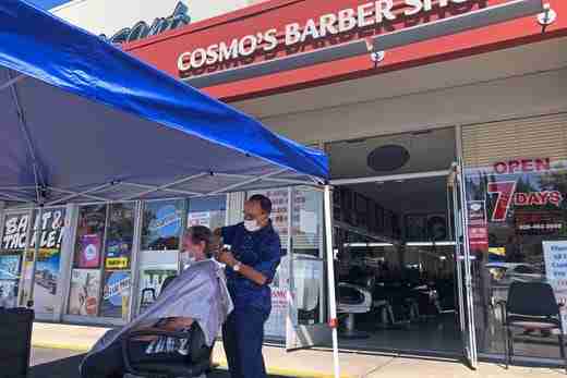A customer of Cosmo's barber shop receives a haircut in the parking lot in front of the shop on Wednesday, July 22, 2020, in Pleasanton, Calif.  Throughout May and June, California reopened much of its economy, and people resumed shopping in stores and dining in restaurants. But infections began to surge and a new round of business restrictions were imposed, including a ban on indoor dining in restaurants and bars.
