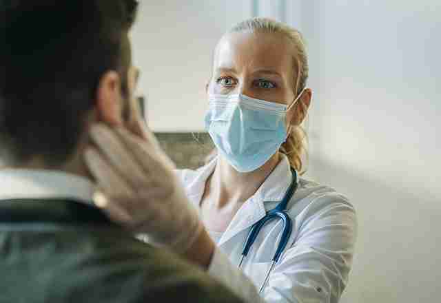 A doctor examines a patient's throat while wearing a mask.