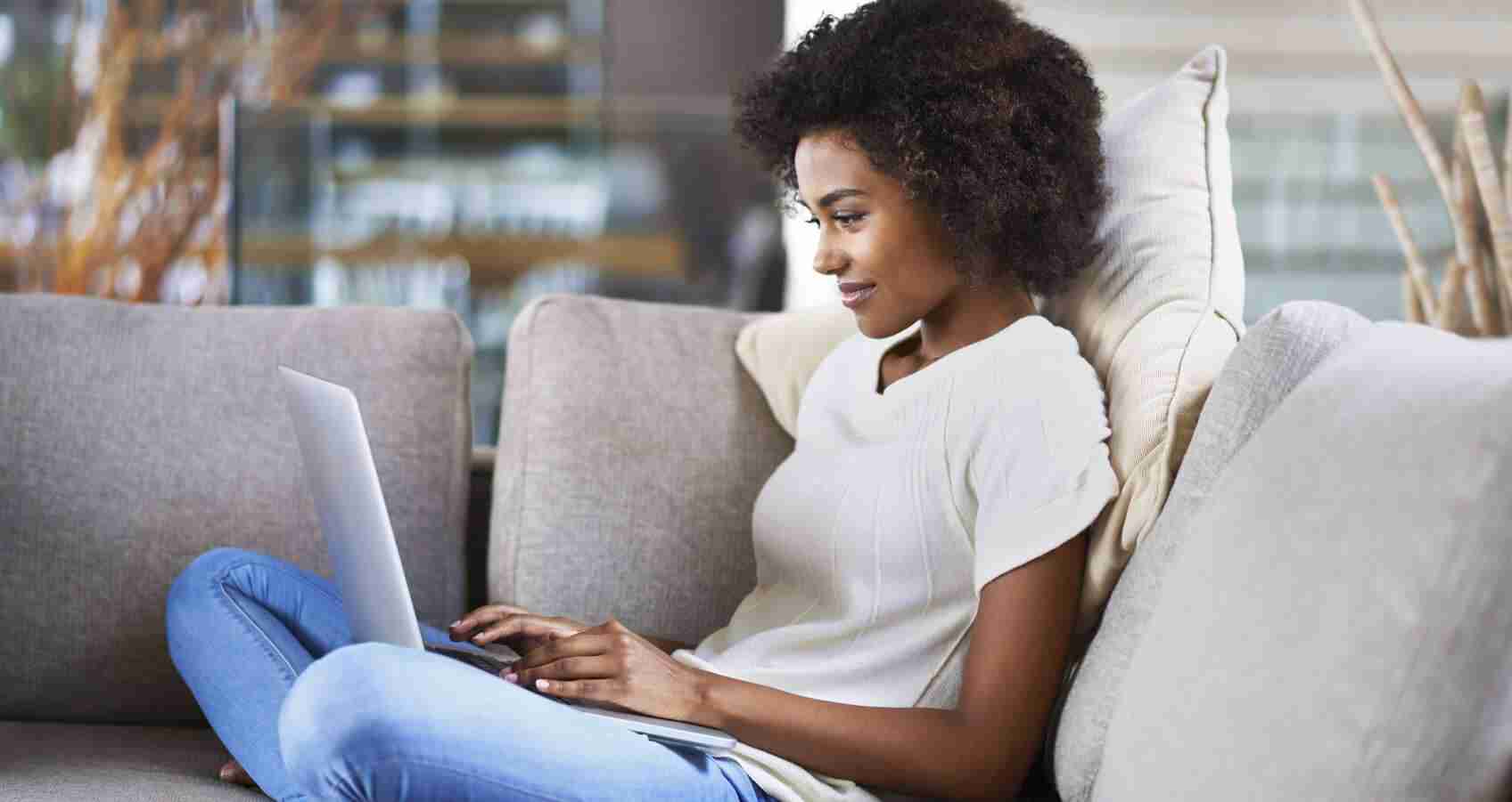 Smiling young woman sitting on couch with a laptop