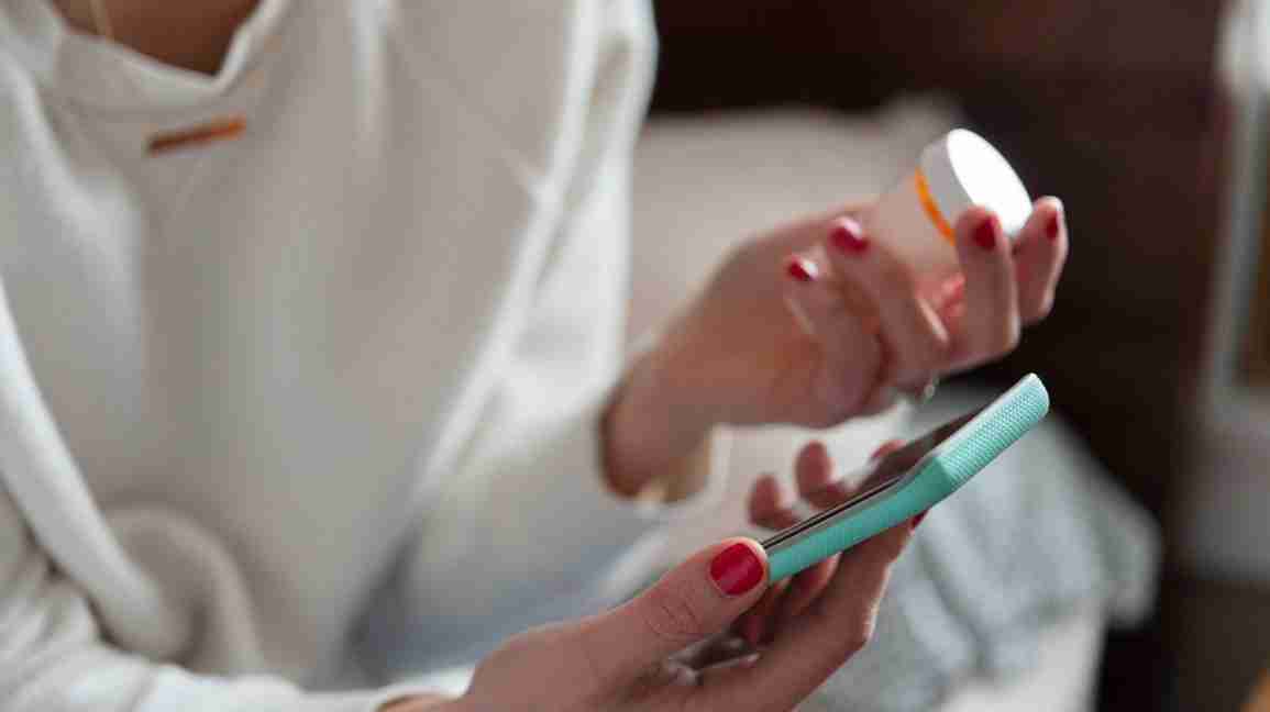 a woman holding a bottle of medication, reading her phone to assess her RA treatment