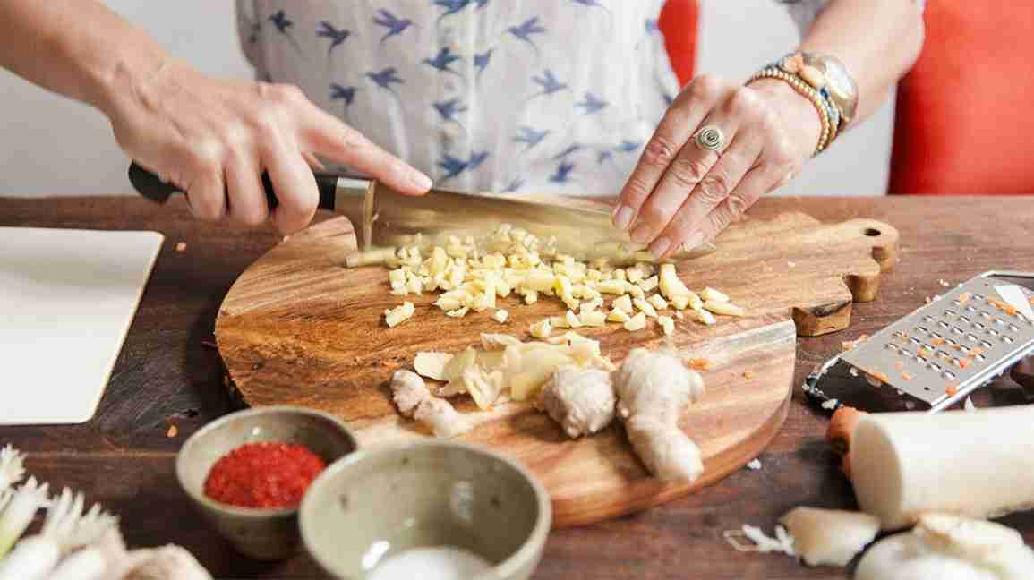 chopping raw ginger root on a wooden cutting board