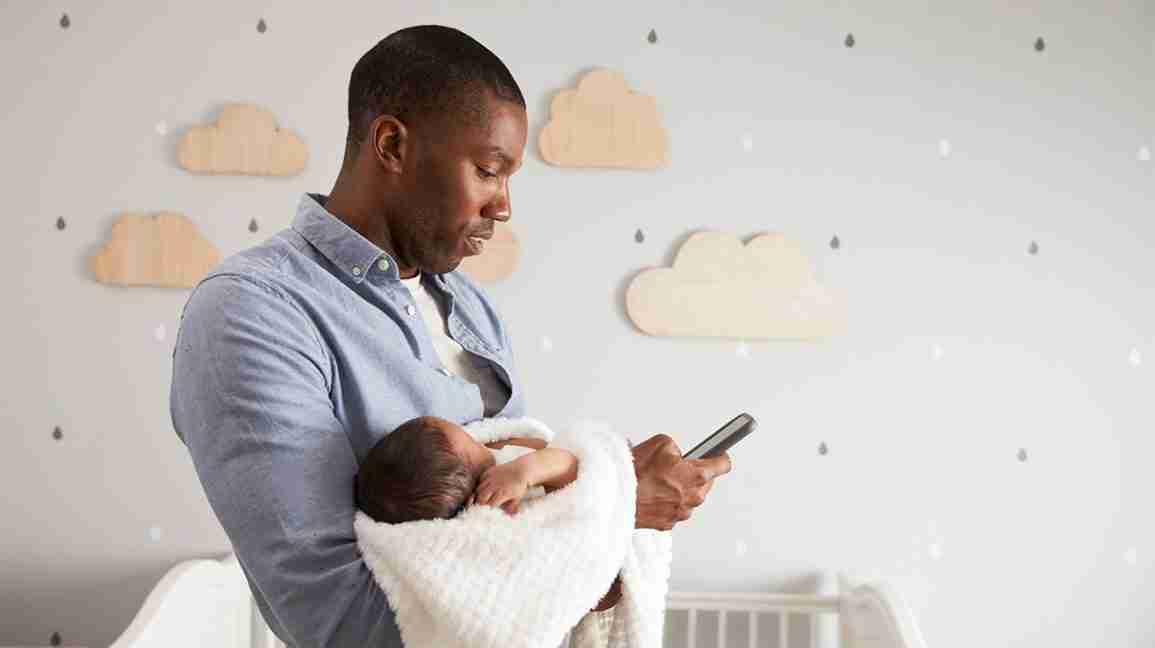 father consults his phone while holding newborn