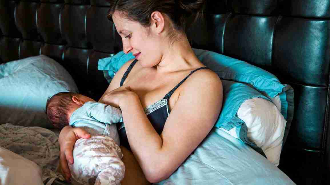 Mother breastfeeding baby on bed