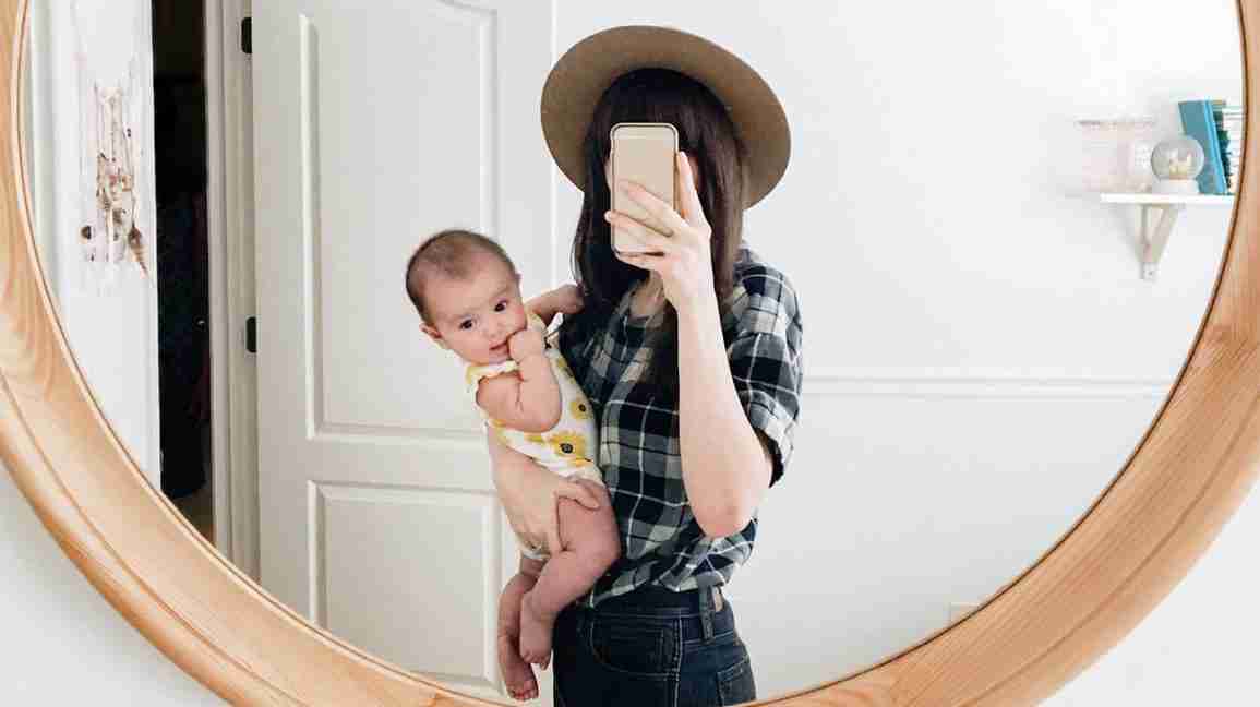 woman holding baby takes mirror selfie