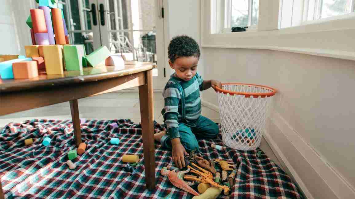 child uses basket to pick up toys