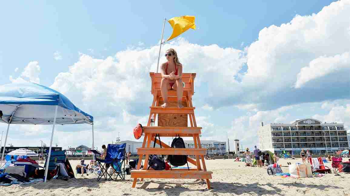 A lifeguard sits on a raised chair above the sand, looking out at the crowded beach