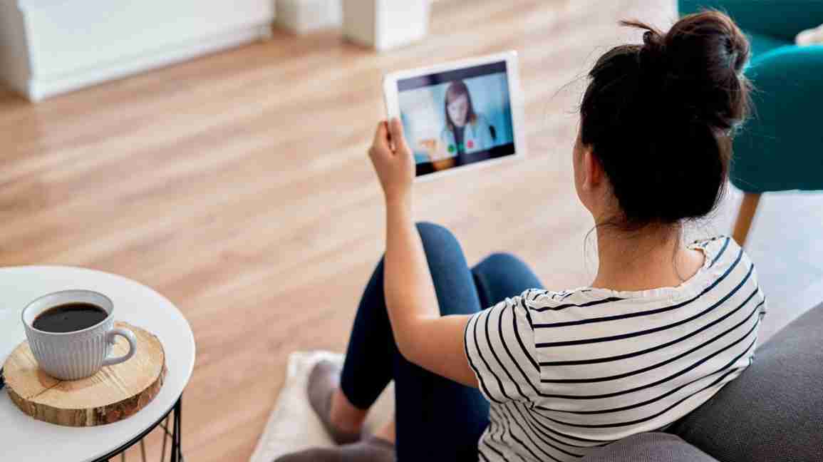 A woman sits on the floor of her living room, while consulting with a therapist online, via an iPad. 