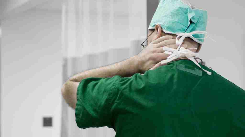 a Physician rubbing the back of his neck because he has pain there from burnout