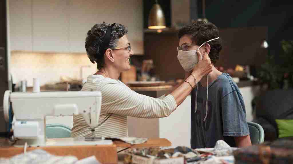 A photo of a mother fitting a face mask to her son to accompany the article "Is COVID-19 more dangerous because it reduces specific microRNAs?"