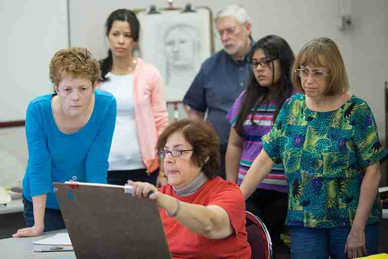 students look over instructor's shoulder as she show's artwork