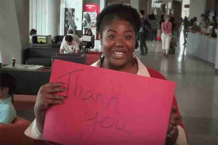 A woman in the Student Union holding up a red sign that reads thank you.